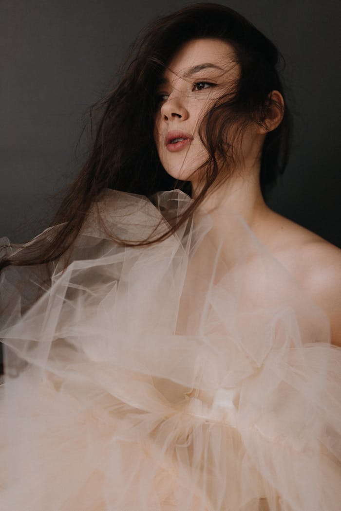 Artistic portrait of a woman enveloped in delicate tulle fabric against a dark backdrop.